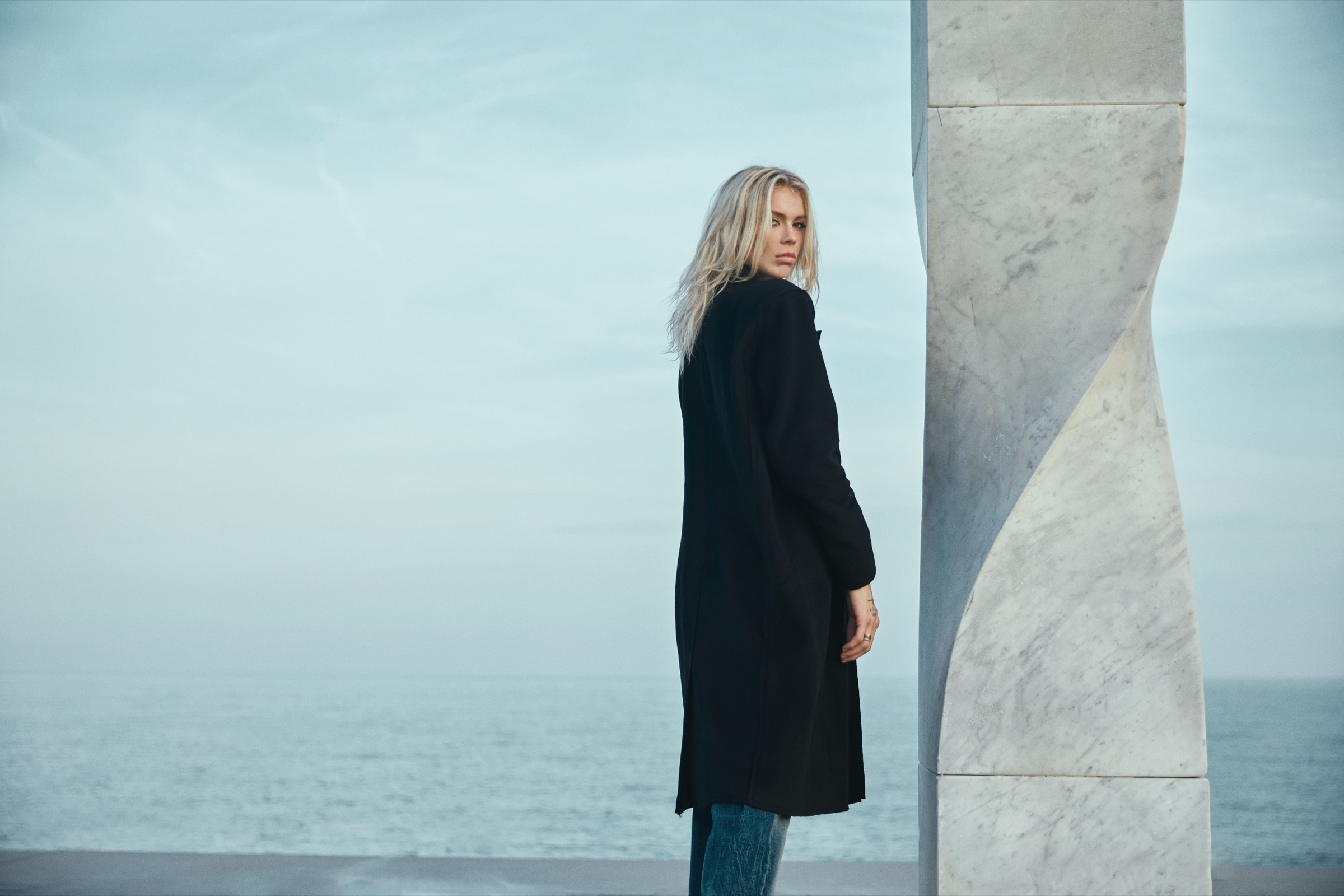 Model in a long black coat by the sea